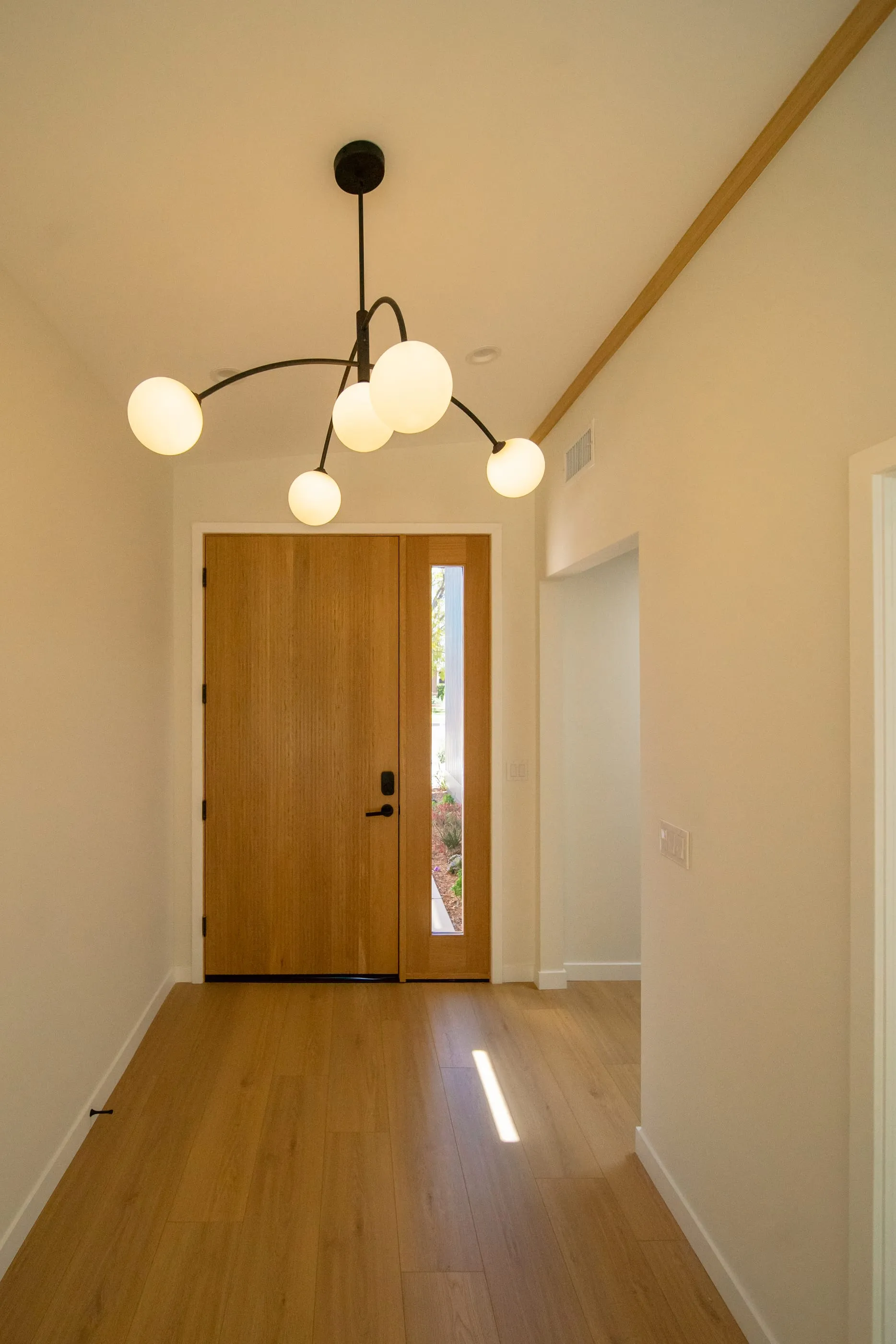 Interior entry hall with oak door, oak floor, and sculptural globe chandelier