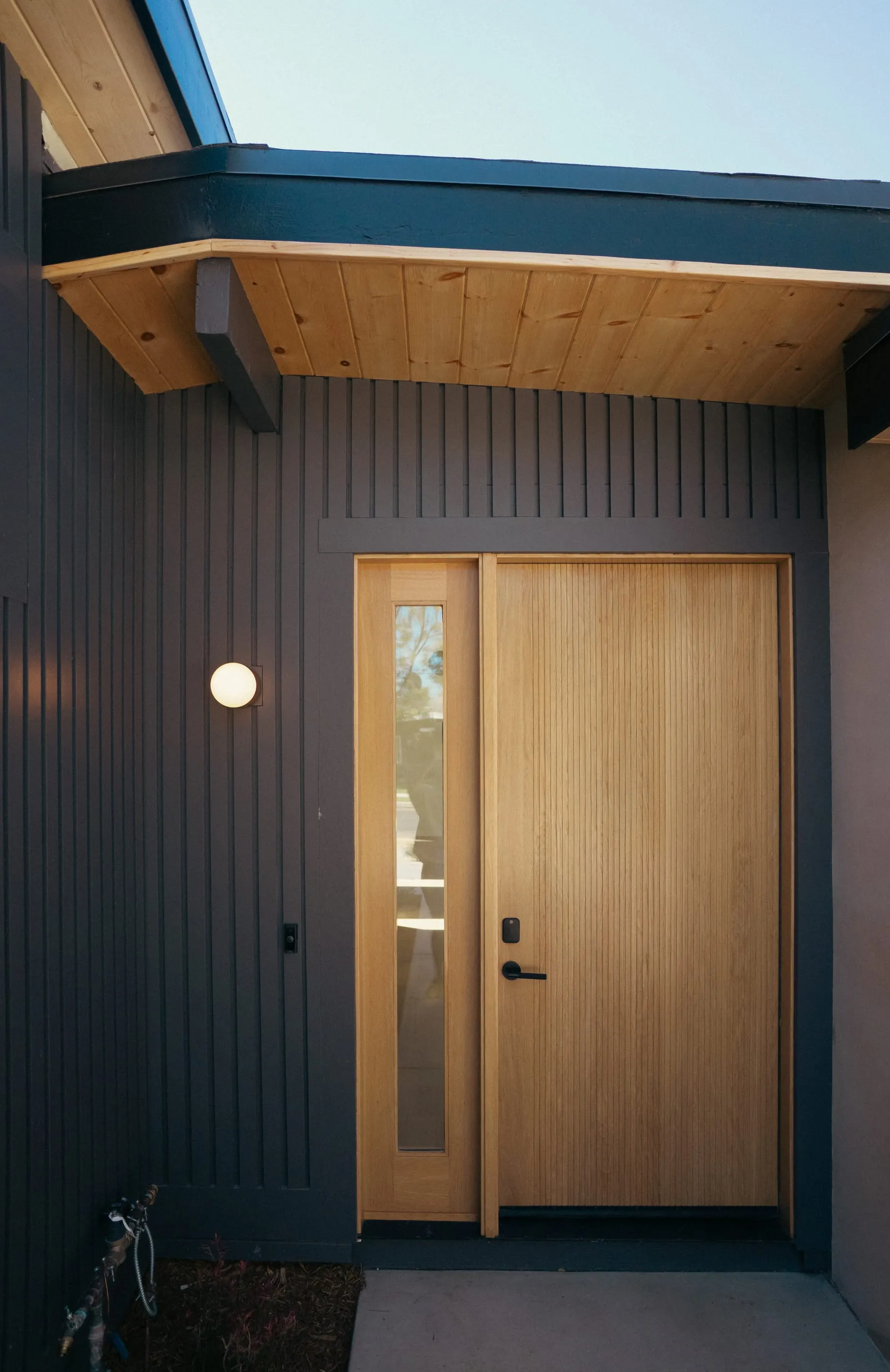 Oak front door beneath a wood soffit and globe sconce