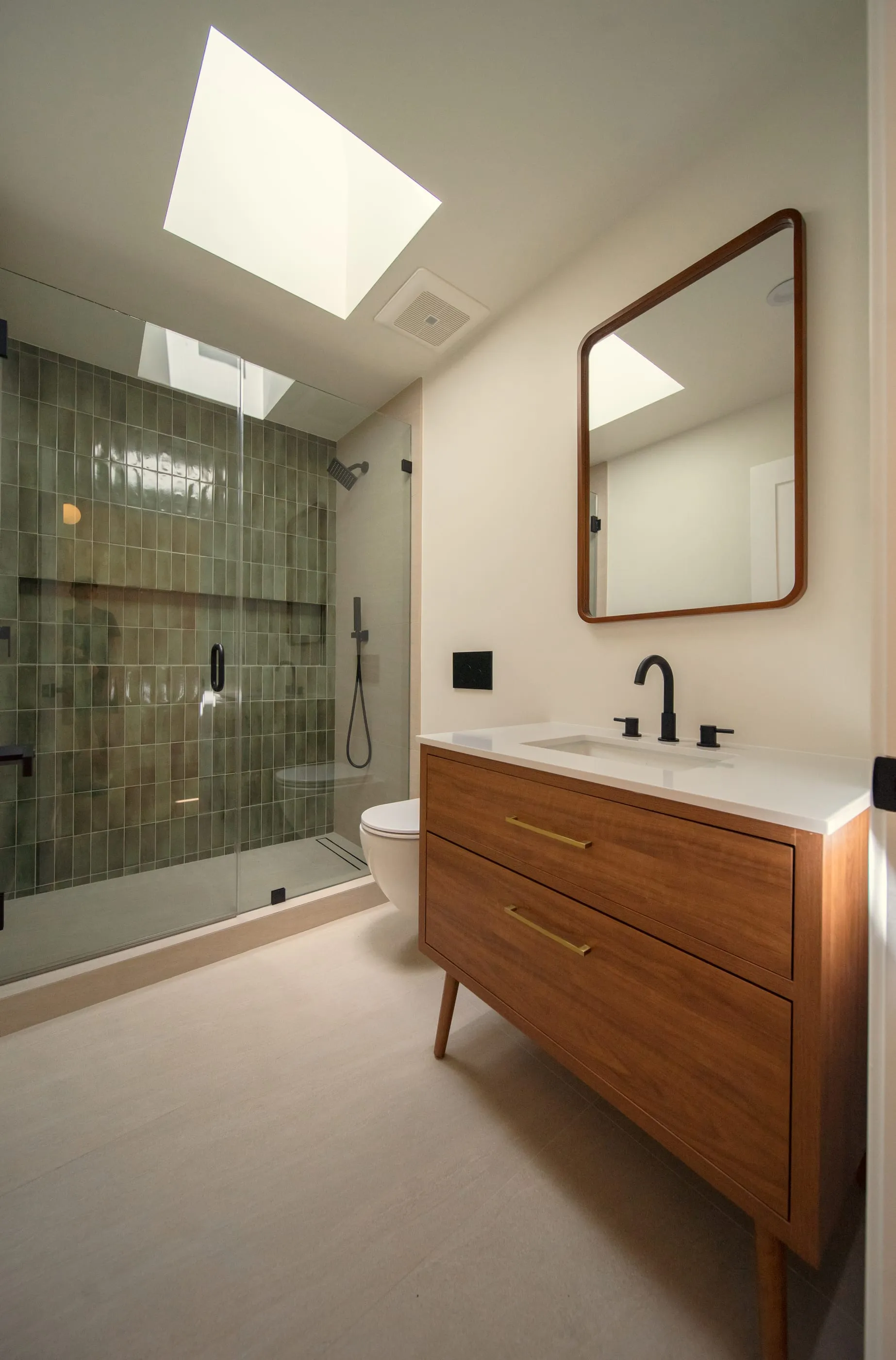 Bathroom with green textured shower tile, walnut vanity, and a skylight