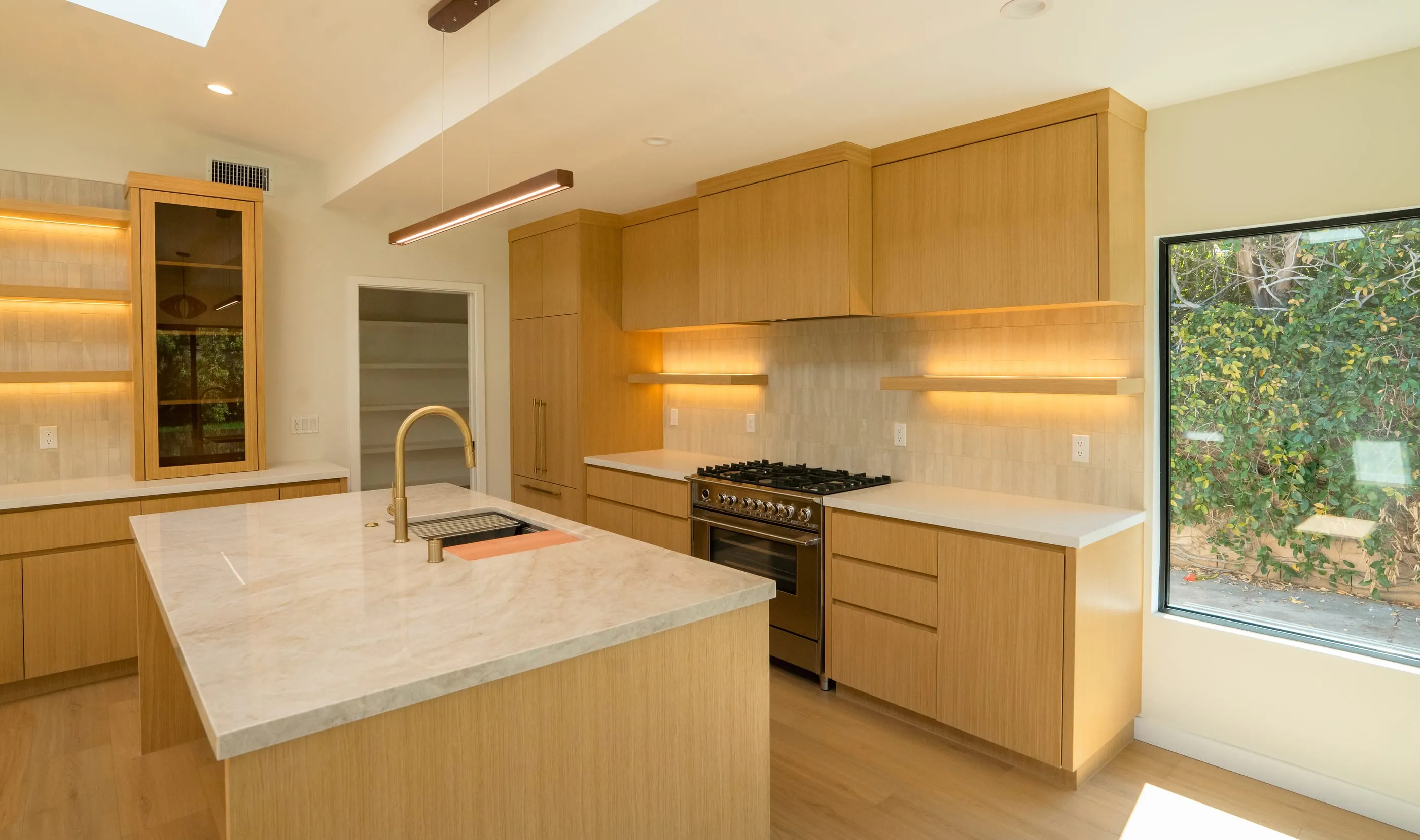 Reverse kitchen view showing oak cabinetry, illuminated shelves, and the island