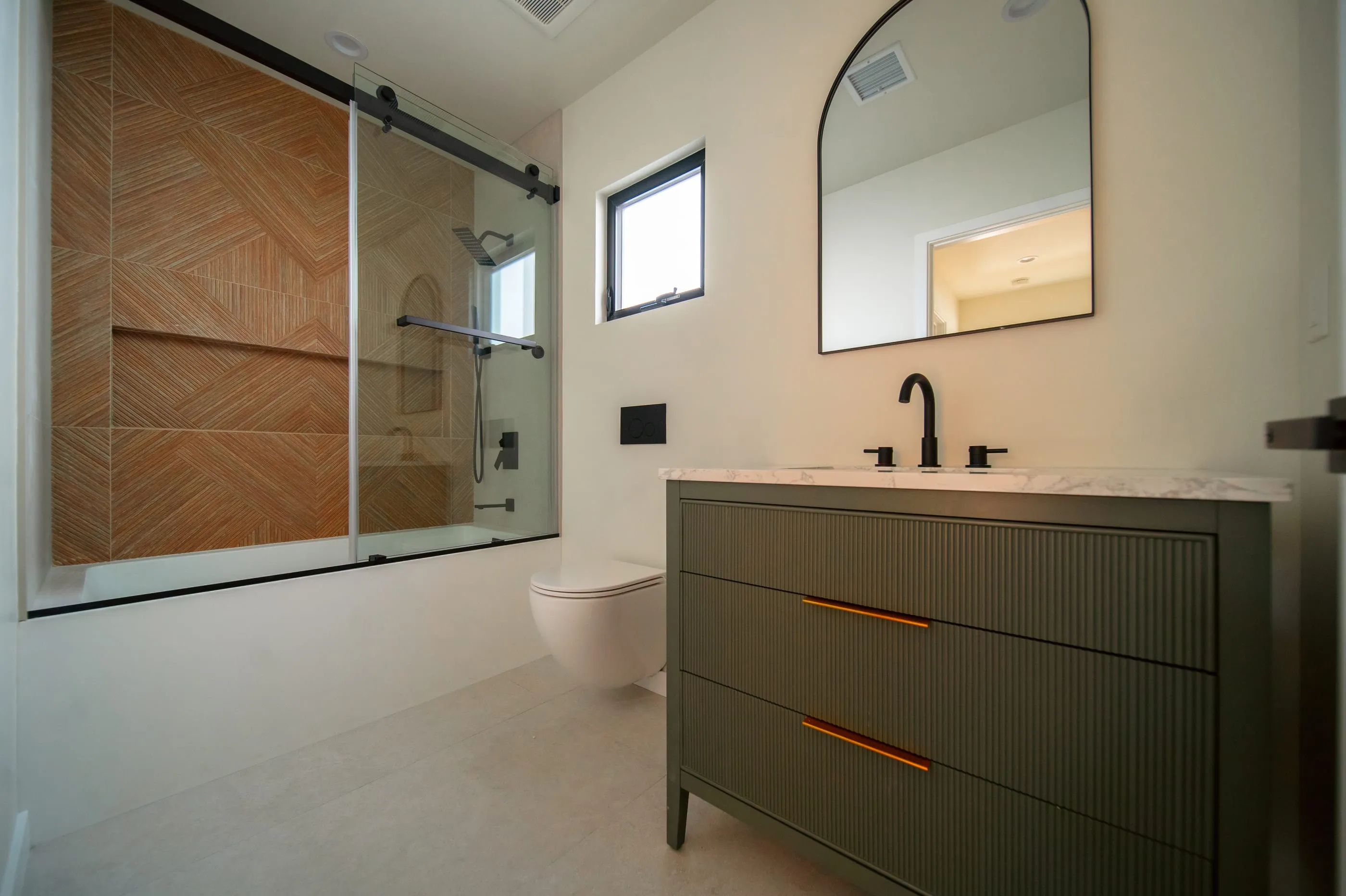 Bathroom with geometric wood-toned shower tile and a dark reeded vanity