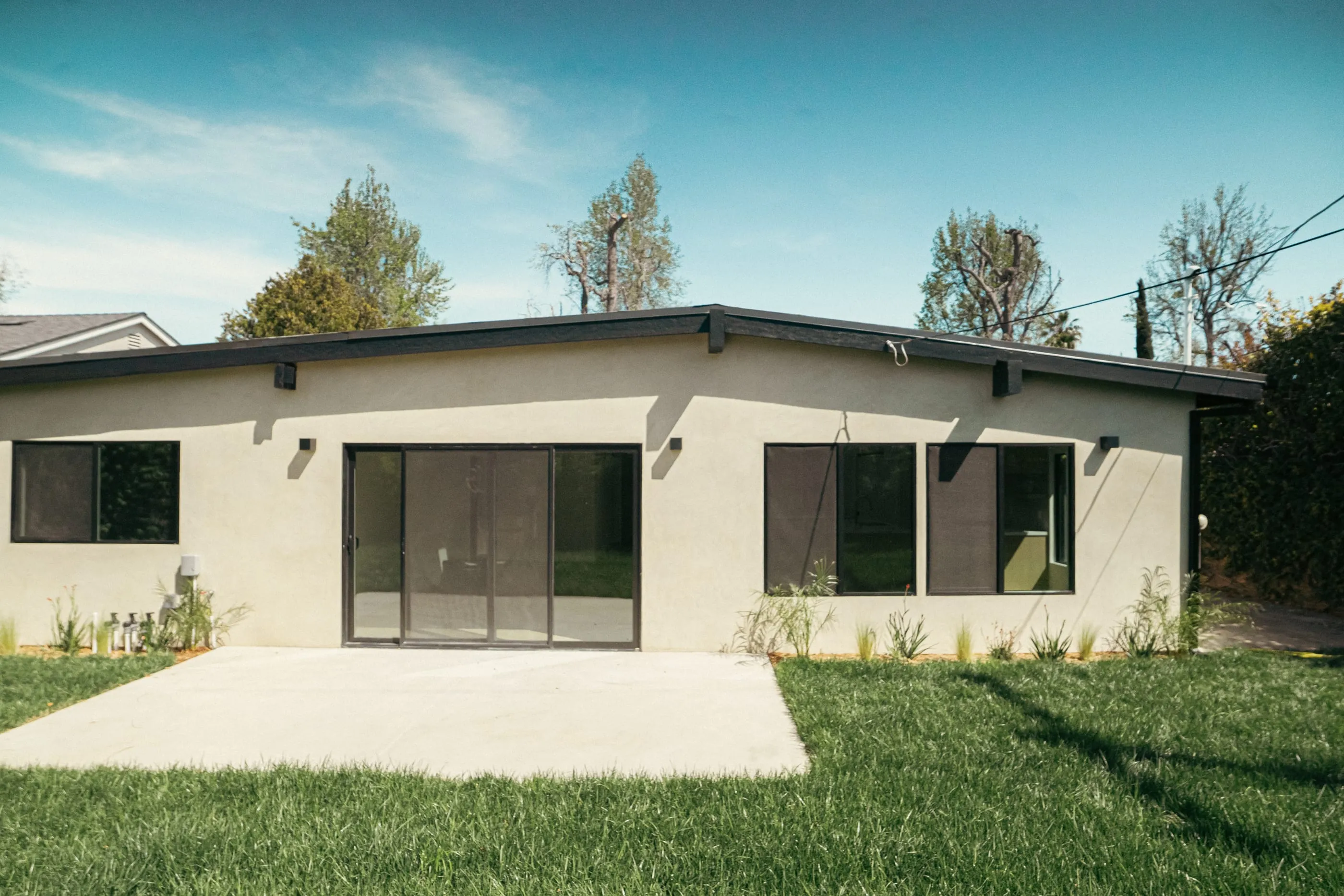 Rear elevation with a low roofline, dark-framed openings, patio, and lawn