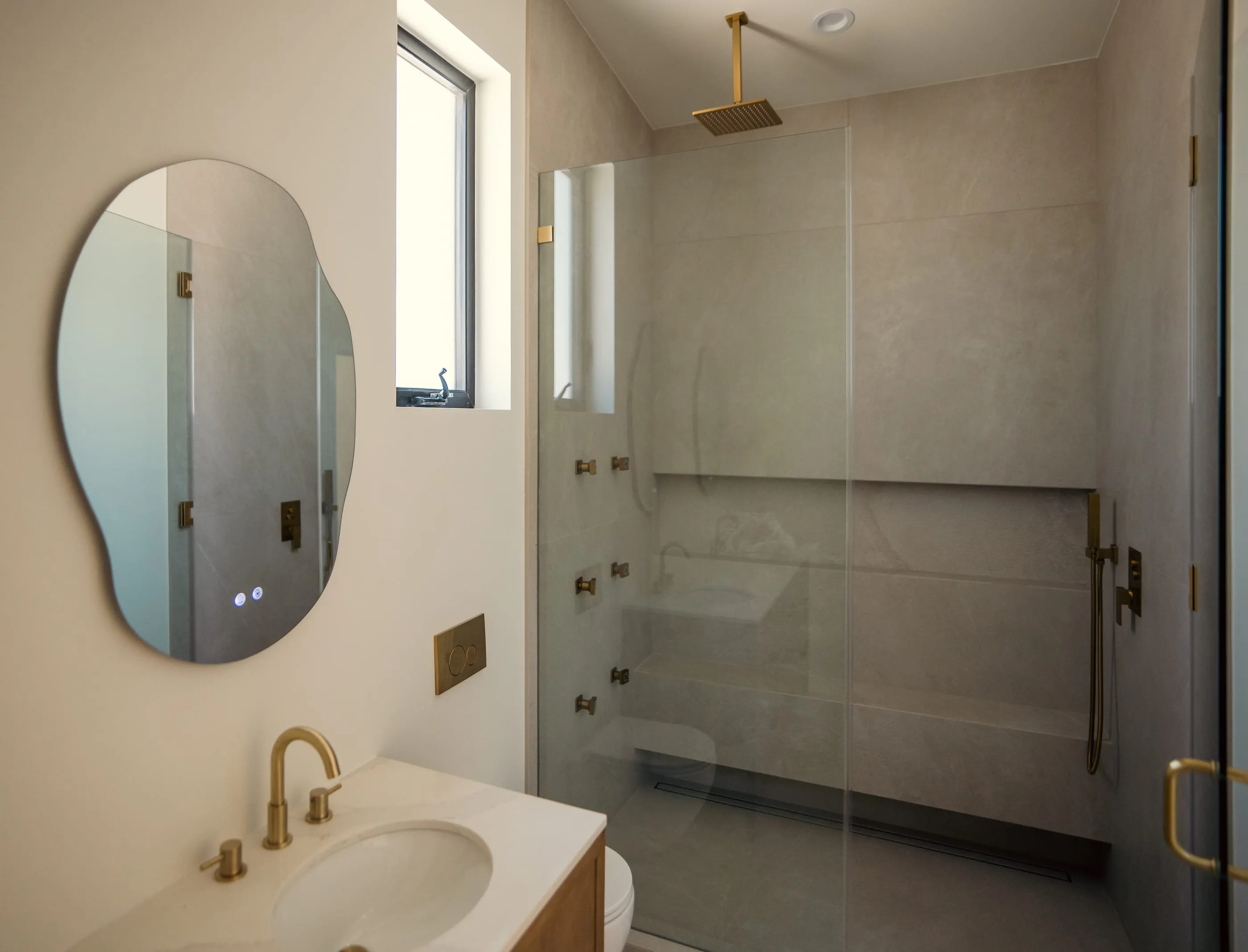Bathroom with large-format stone shower surfaces, brass fittings, and an organic mirror