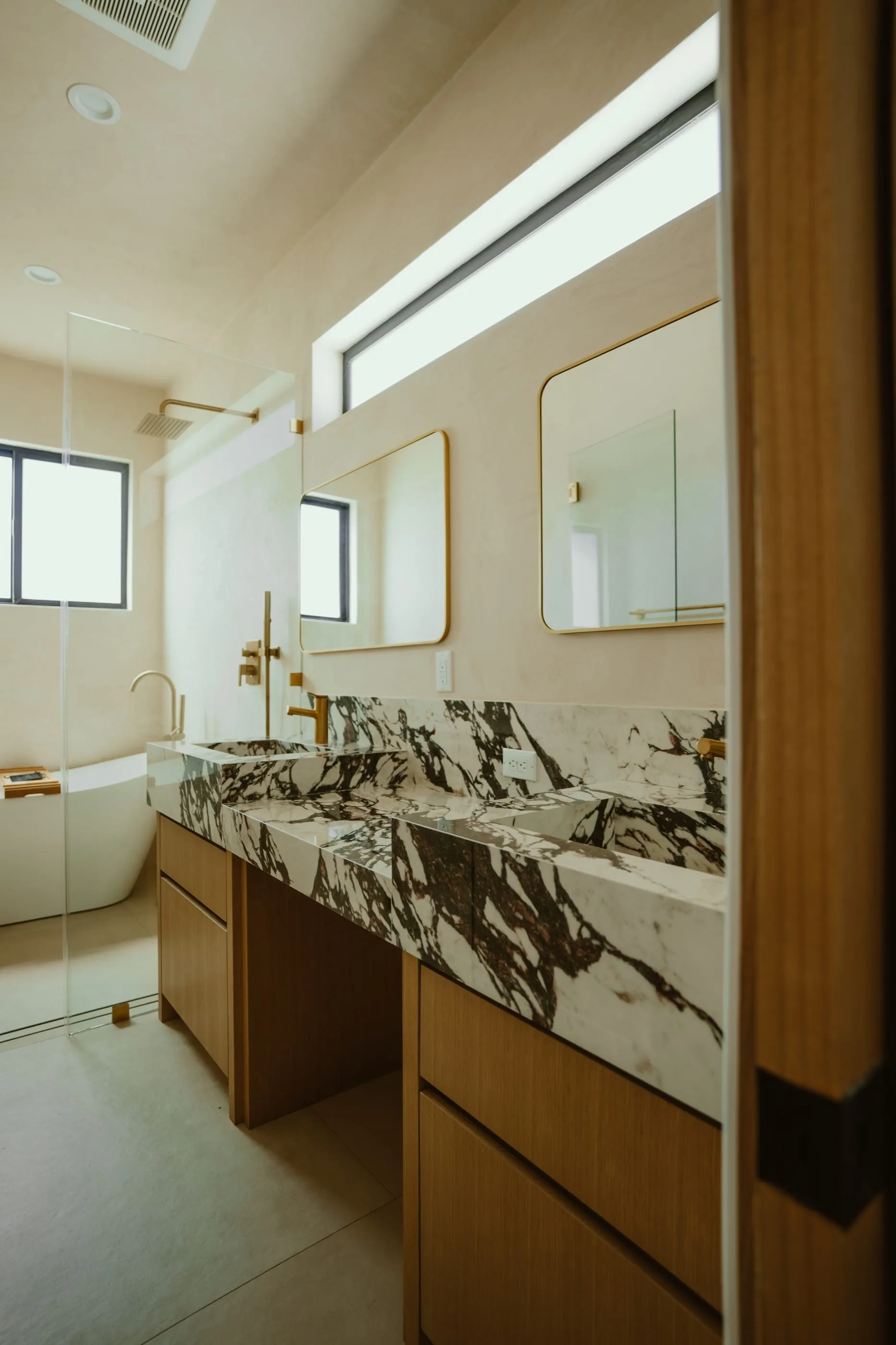 Bathroom with dramatic stone vanity, oak cabinetry, brass fixtures, and freestanding tub