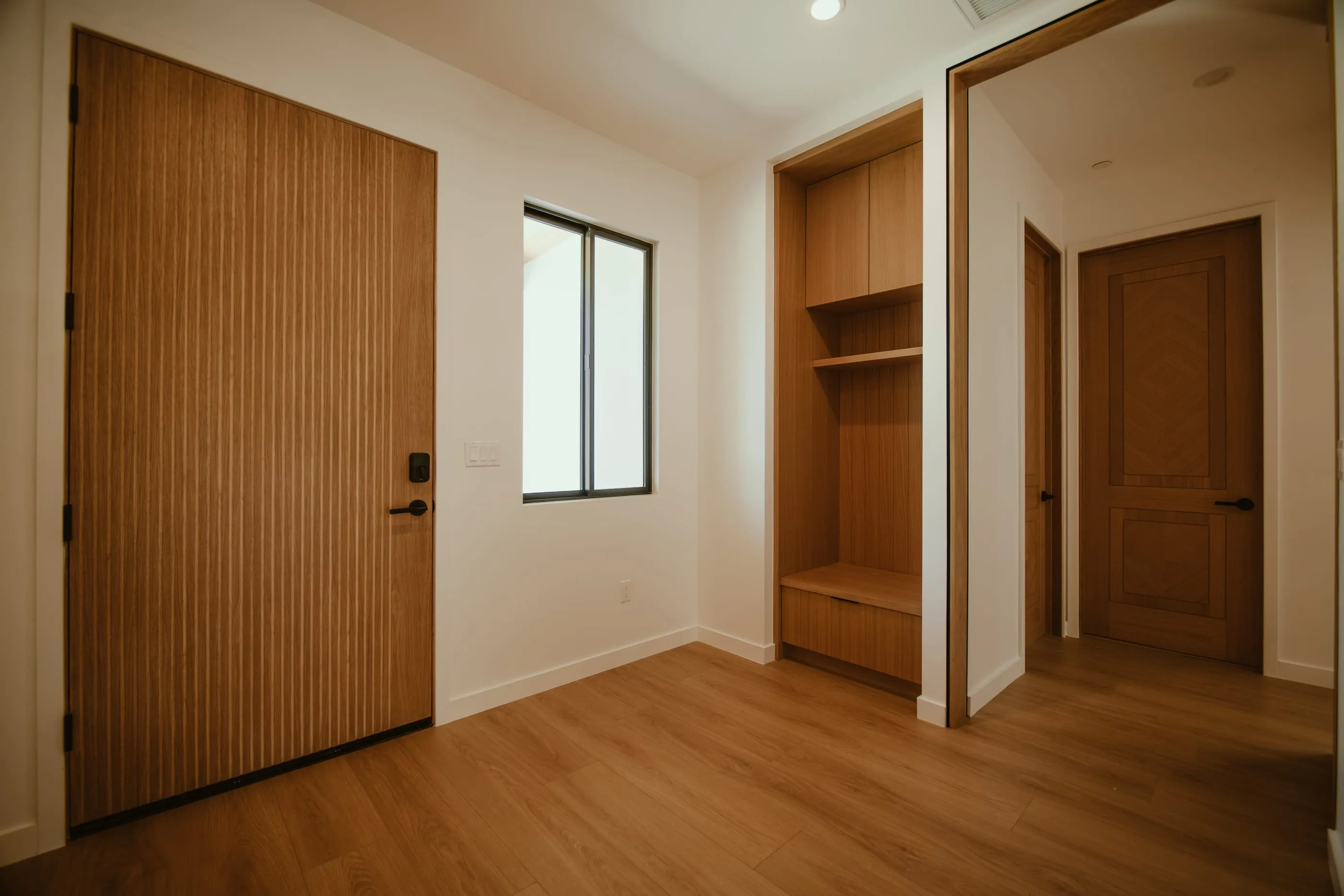 Oak entry door, built-in bench, and full-height mirror opening toward the interior hallway