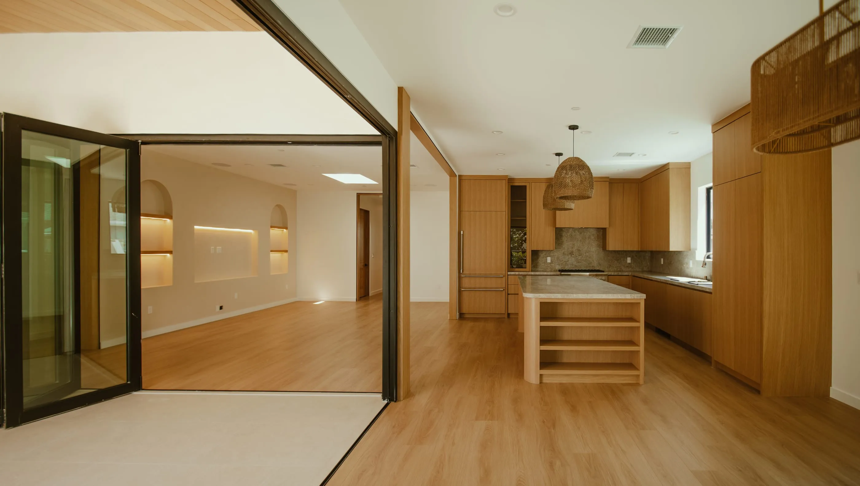 Wide view from the covered courtyard through folding glass doors into the oak kitchen and living space