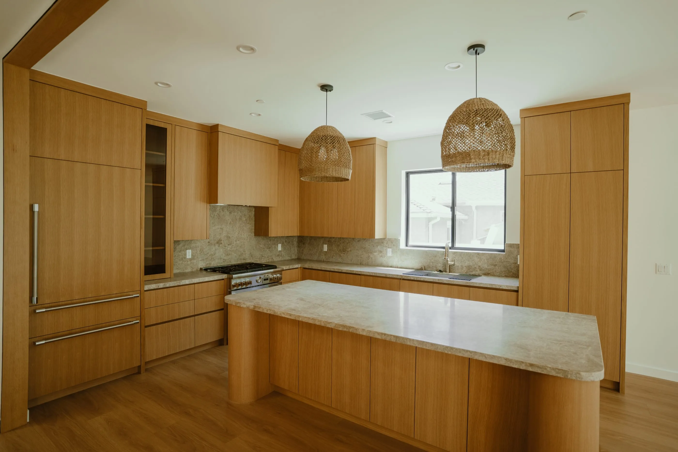 Oak kitchen with rounded island ends, stone counters, and woven pendant lights