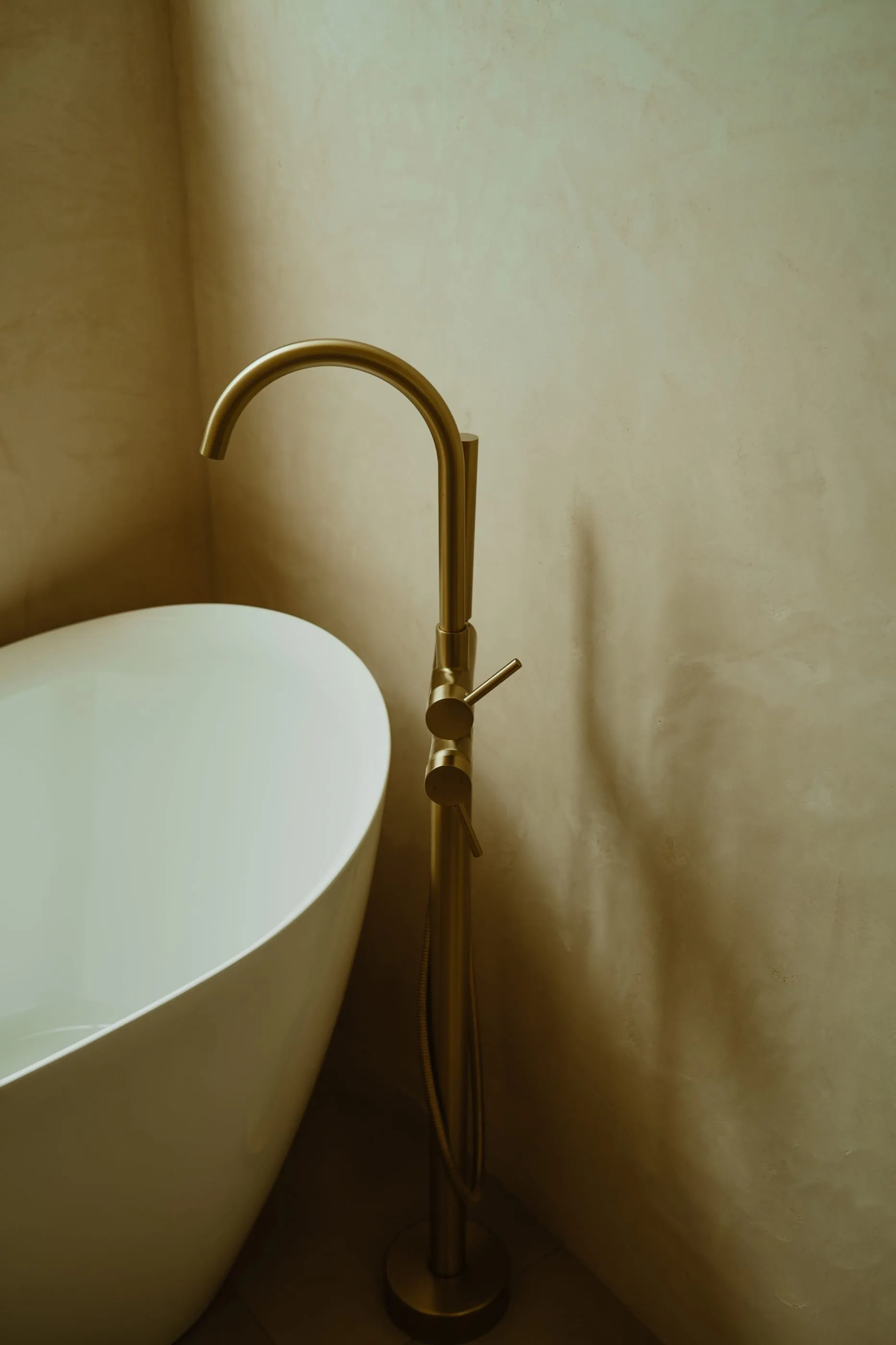 Brass floor-mounted tub filler beside a freestanding white bathtub