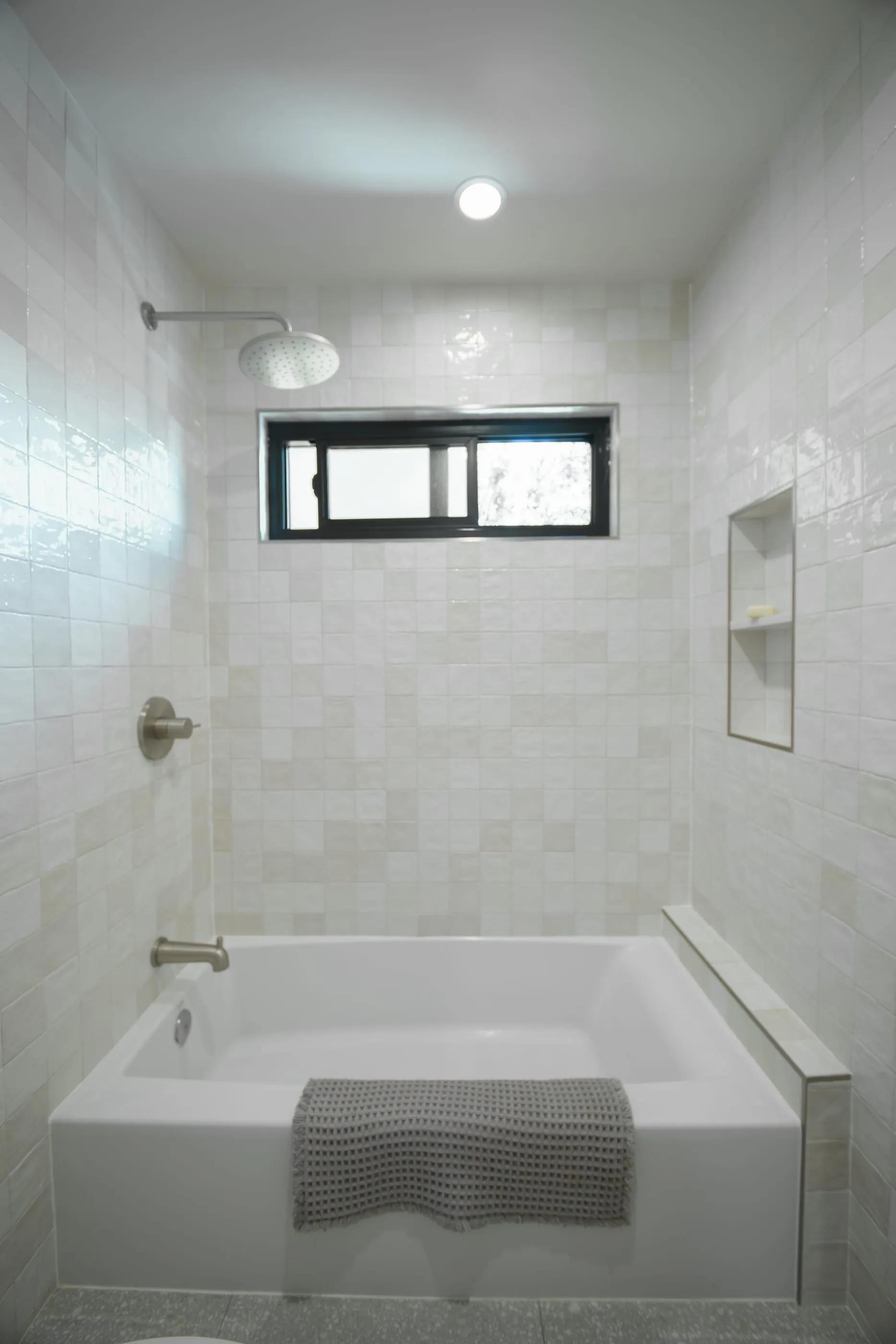 White tiled tub and shower with a dark-framed clerestory window