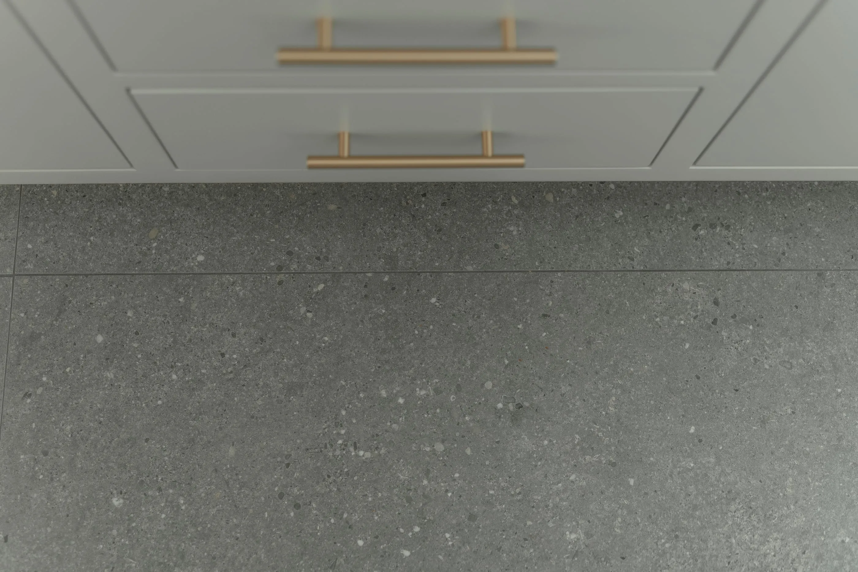 Brass cabinet pulls above large-format gray stone floor tile