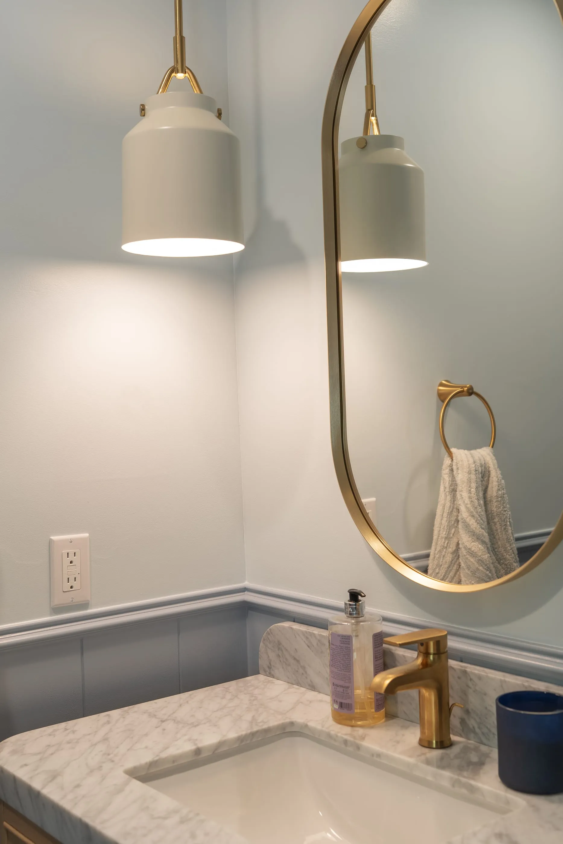 Close view of the brass pendant, arched mirror, and marble vanity