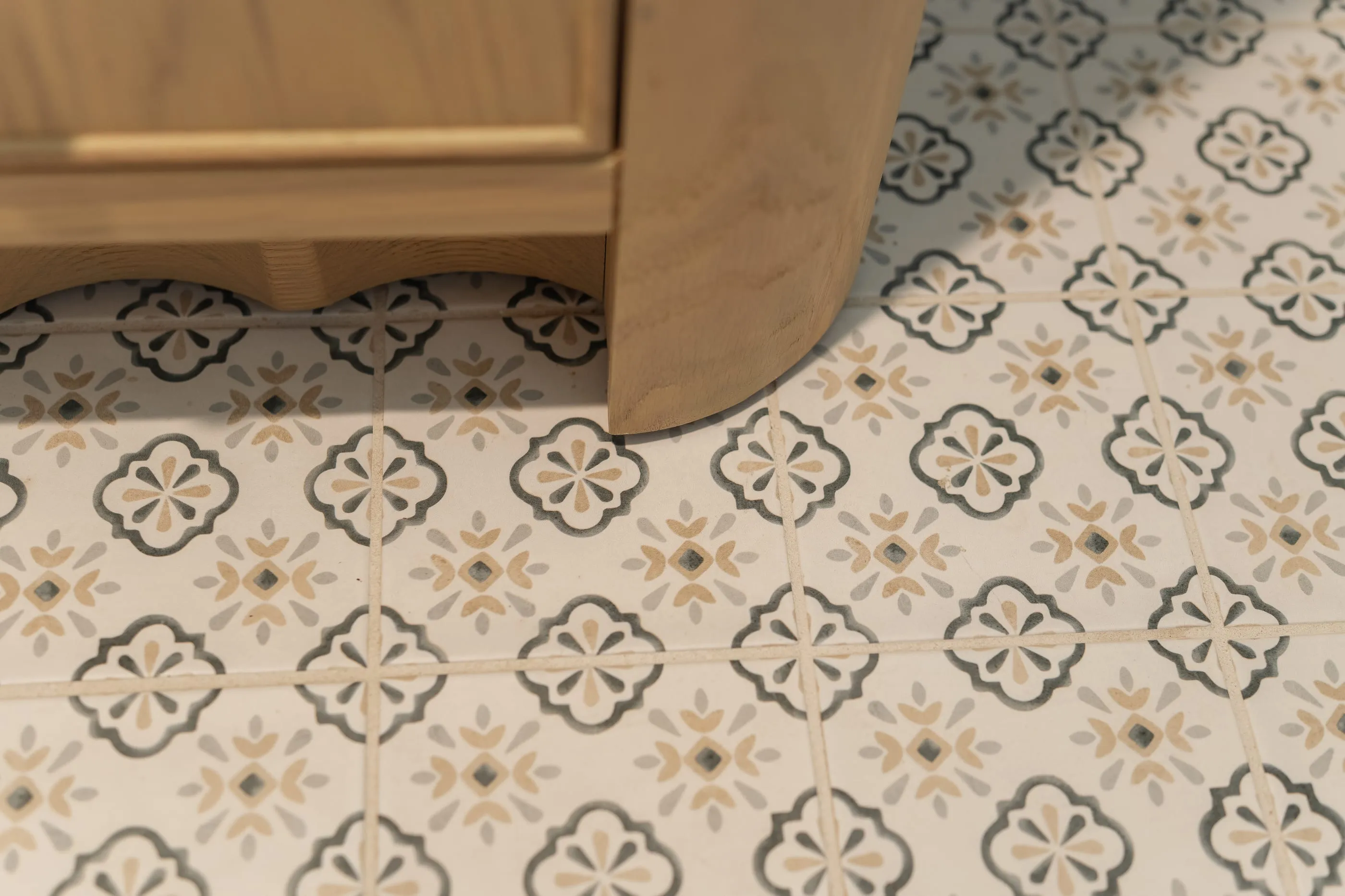 Patterned floor tile meeting the curved foot of an oak vanity